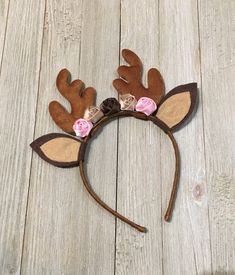 a brown and pink deer headband with flowers on it's ears, sitting on a wooden floor