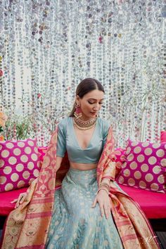 a woman sitting on top of a pink couch wearing a blue and gold lehenga