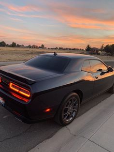 a black sports car parked on the side of the road at sunset or sunrise time