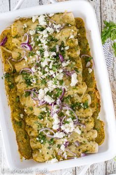 an enchilada with onions, cheese and herbs in a white casserole dish