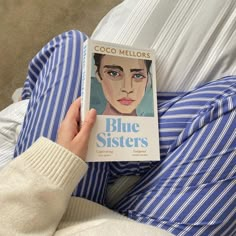 a person sitting on a bed with a book about blue sisters in front of them