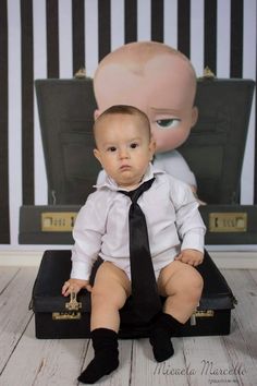 a baby sitting on top of a suit case wearing a black tie and white shirt