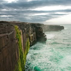 an ocean cliff with waves crashing against the rocks and green algae growing in the water