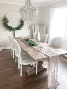 a dining room table with white chairs and greenery