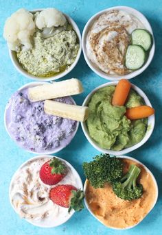 four bowls filled with different types of food on top of a blue countertop next to carrots, broccoli and cucumbers