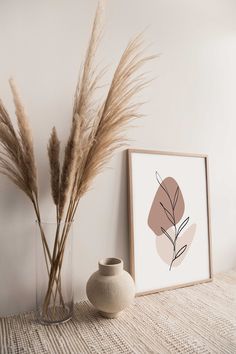 a vase with some dry grass in it next to an art print on the wall