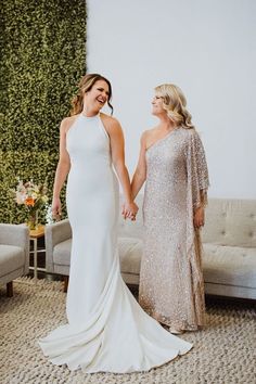 two women holding hands in front of a couch and wall with greenery on it