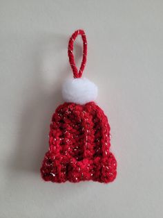 a red knitted bell ornament hanging on a white wall in the shape of a santa hat