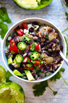 a white bowl filled with black beans and veggies next to sliced avocado