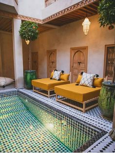 an indoor swimming pool with yellow couches and potted plants on the side wall