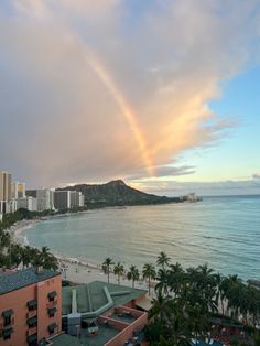 a rainbow in the sky over a beach next to some buildings and water with palm trees