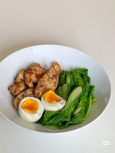 an egg, lettuce and chicken are in a white bowl on a table