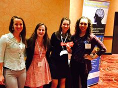 four women standing next to each other in front of a table with a poster on it