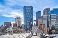 a city skyline with tall buildings and a bridge in the foreground on a sunny day