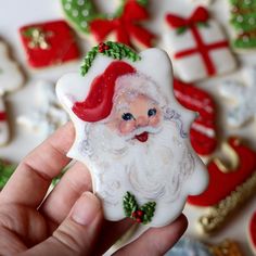 a hand holding a decorated christmas cookie with santa clause on it's face and other cookies in the background