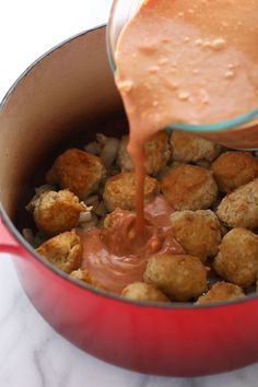 a red pot filled with meatballs and sauce being poured into the pan to cook them