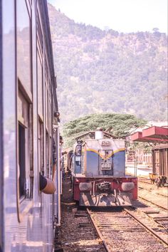 the train is stopped on the railroad tracks next to the building and mountains in the background