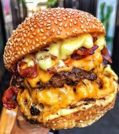 a hand holding a cheeseburger with bacon and other toppings