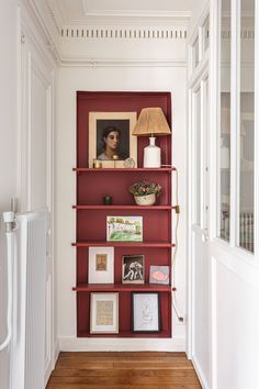 a red book shelf with pictures on it in the hallway next to a radiator