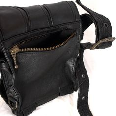 a black leather purse with zippers on the front and side pockets, sitting on a white surface