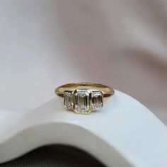 a three stone diamond ring sitting on top of a white cloth