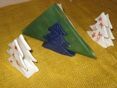 three small ceramic christmas trees sitting on top of a yellow cloth covered table next to each other