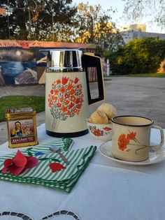 a table topped with a coffee pot next to a cup and saucer on top of a white table cloth