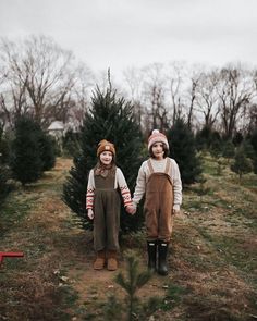 two young children standing next to each other in front of a christmas tree at the farm