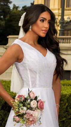 a woman wearing a wedding dress and holding a bouquet in front of a large building