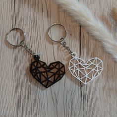 two heart shaped wooden key chains sitting next to each other on a wood table with feathers