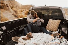 two people sitting in the back of a pick up truck with blankets on the bed