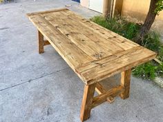 a wooden table sitting on the side of a road next to a tree and building