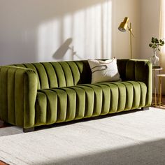 a green couch sitting on top of a rug in a living room next to a lamp