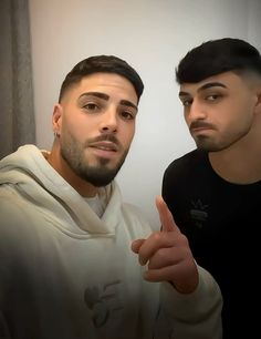 two young men standing next to each other in front of a mirror with one pointing at the camera