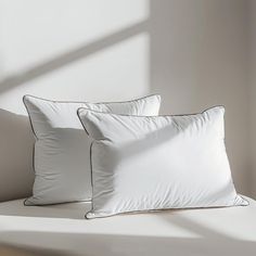 two white pillows sitting on top of a bed next to each other in front of a window