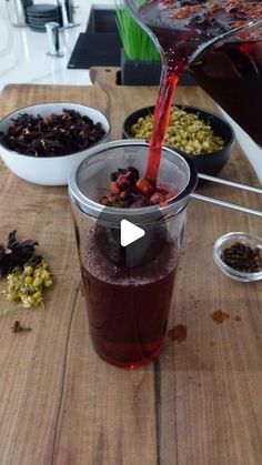 a person pours red liquid into a cup on a wooden table with bowls of food in the background