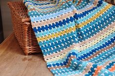 a crocheted blanket sitting on top of a wooden table next to a basket