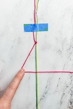 a hand is pointing at a piece of colored paper on a marble surface with red and blue tape