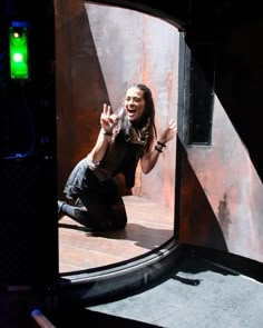 a woman sitting on the ground in front of a metal wall with her hands up