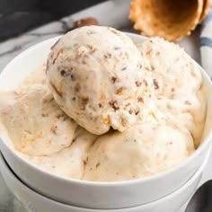 two scoops of ice cream in a white bowl on a marble surface with an orange napkin