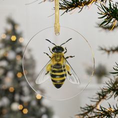 a glass ornament with a yellow and black bee on it hanging from a christmas tree