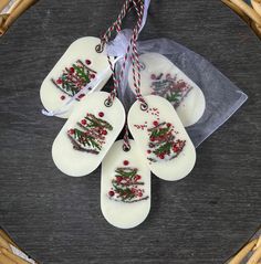 four white ceramic spoons with christmas decorations on them hanging from twine strings in a wicker basket