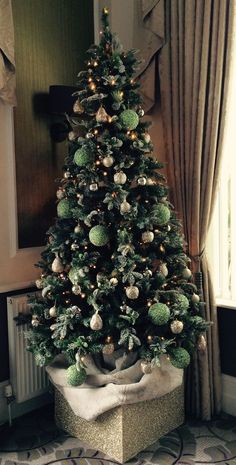 a decorated christmas tree in a living room next to a window with curtains and drapes