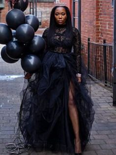 a woman in a black dress is standing on the sidewalk with some balloons behind her