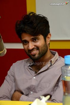 a man sitting at a table with a bottle in front of him and a microphone to his side