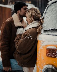 a man and woman kissing in front of an old vw bus covered in snow