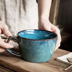 a person holding a blue cup on top of a wooden table