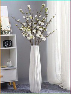 a white vase filled with flowers on top of a blue rug next to a window