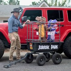 a man standing next to a red truck with kids in it's cage on the back