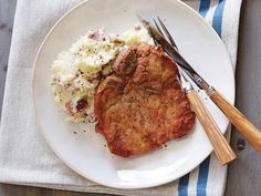 a white plate topped with meat and mashed potatoes next to a knife and fork